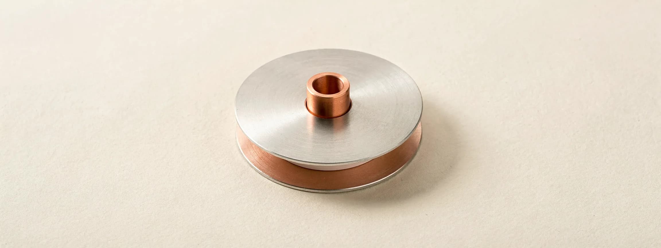 A brushed steel ticker-tape reel on a copper spool, on paper.