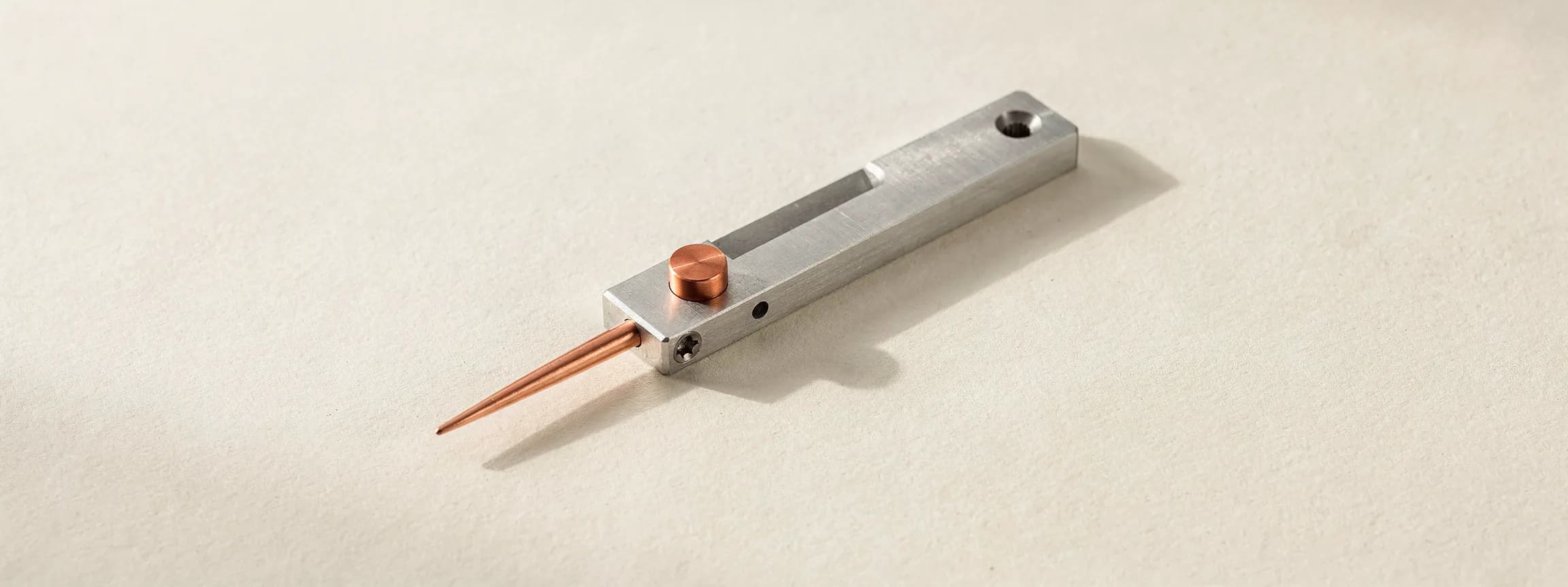 A machined steel scoring gauge with a copper pointer, on paper.
