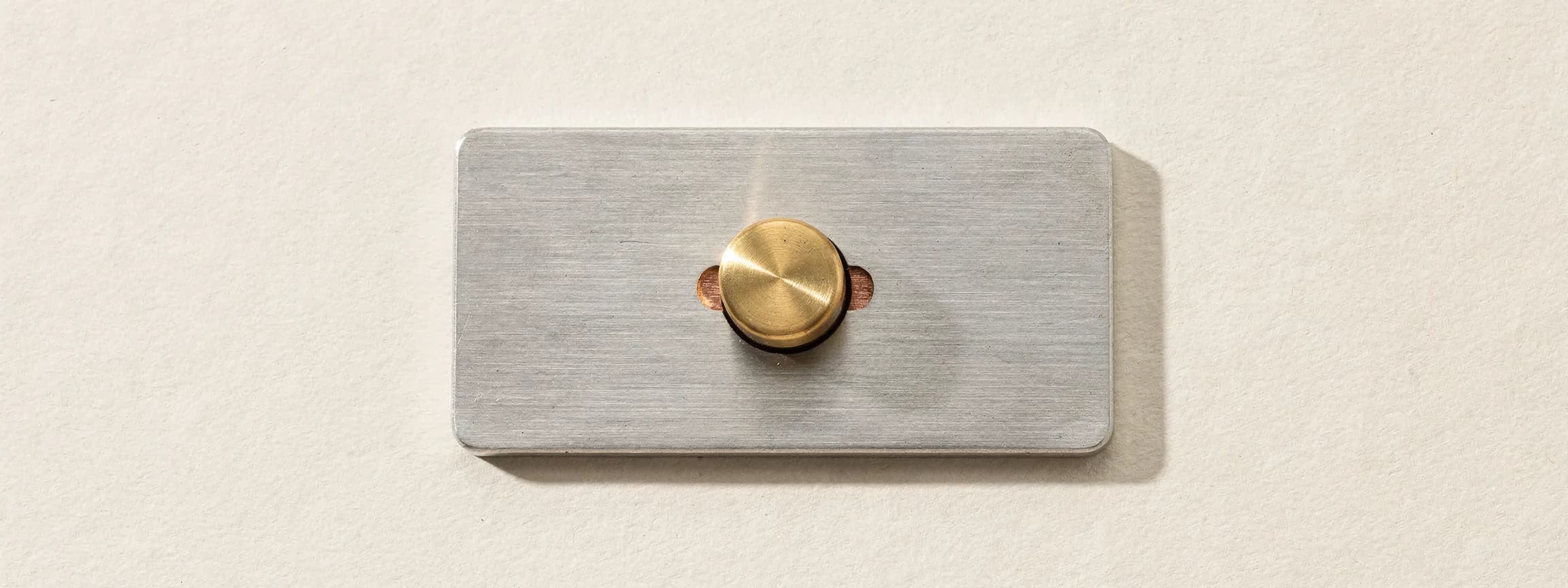 A brass door-bell button set in a brushed steel plate, on paper.