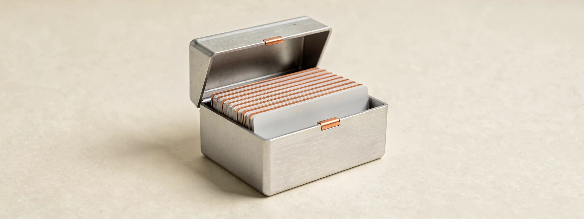 A steel card-index box with copper tabs, lid open, on paper.