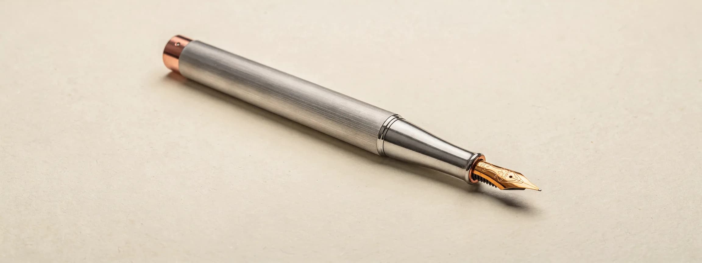 A brushed steel fountain pen with a copper nib, uncapped, on paper.