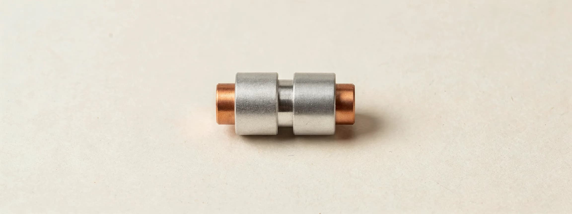 A brushed steel fibre coupler with copper collars, on paper.