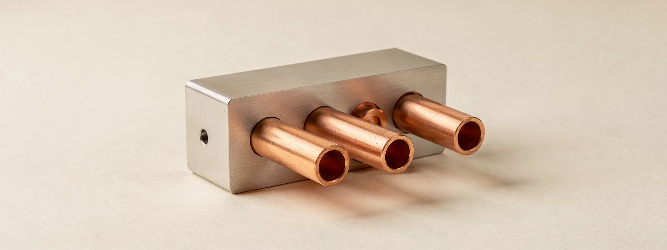 A brushed steel manifold with four copper outlet pipes, on paper.