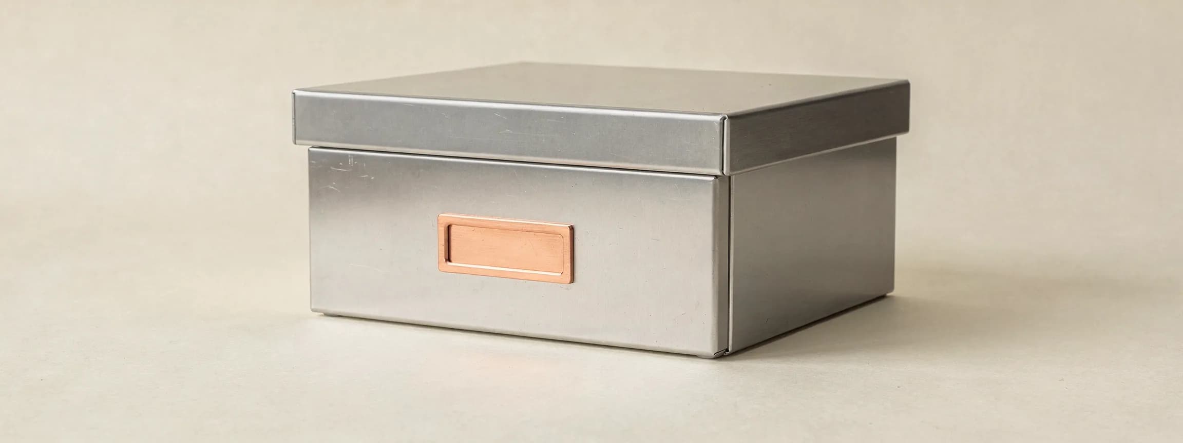 A steel archive box with a copper label frame on its face, on paper.