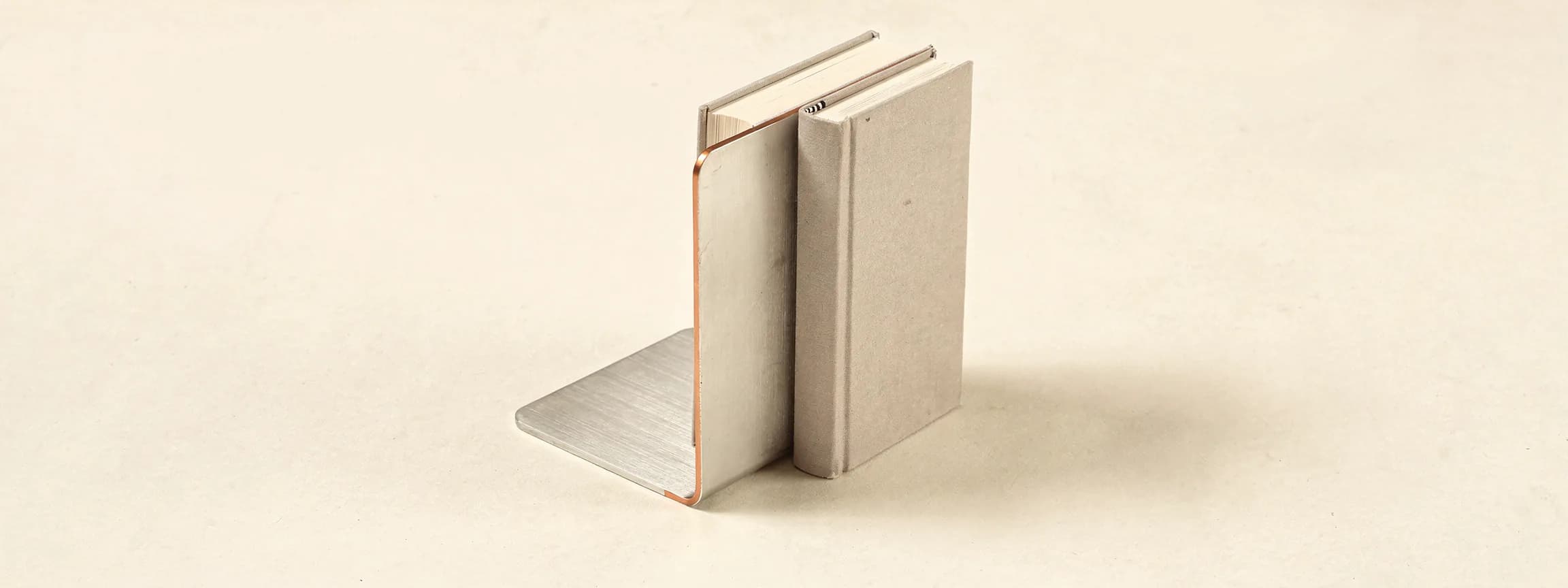 A brushed steel bookend with a copper edge holding two books, on paper.