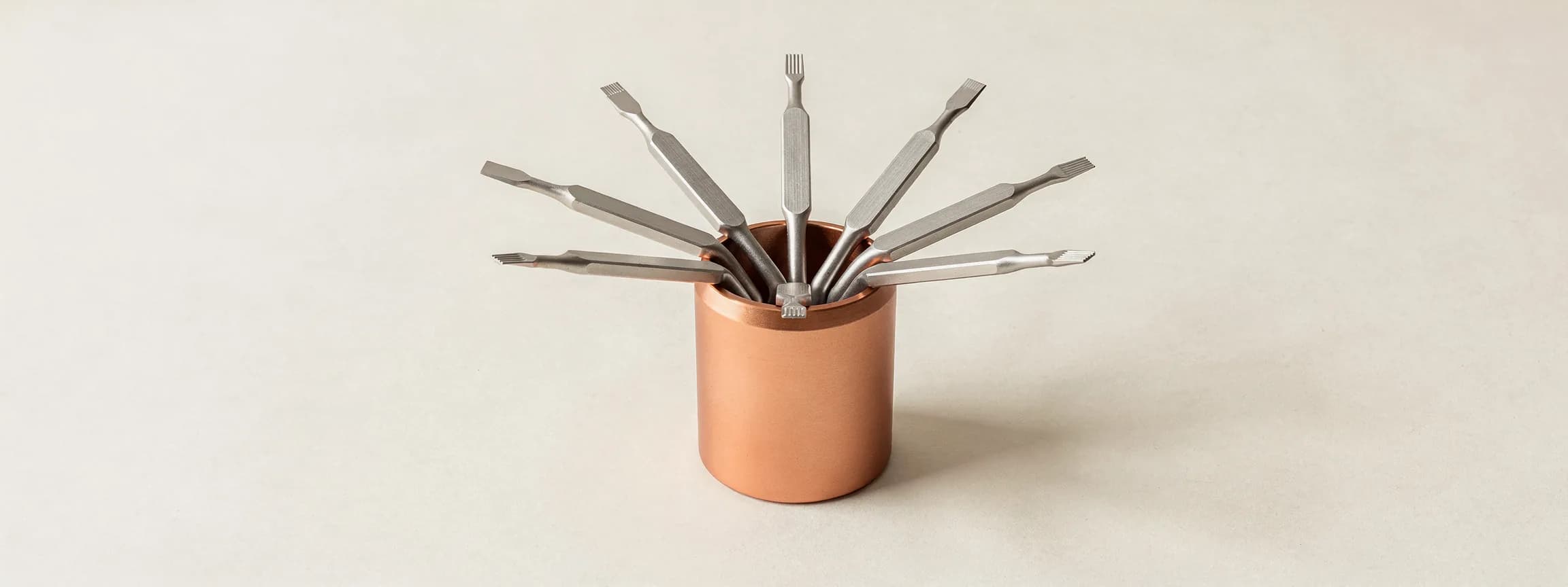 A set of steel screwdrivers fanned in a copper holder, on paper.