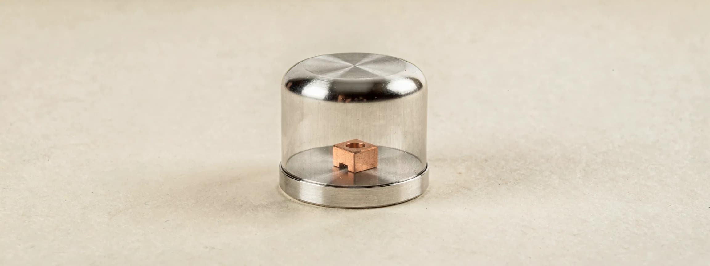 A brushed steel bell jar over one small copper component, on paper.