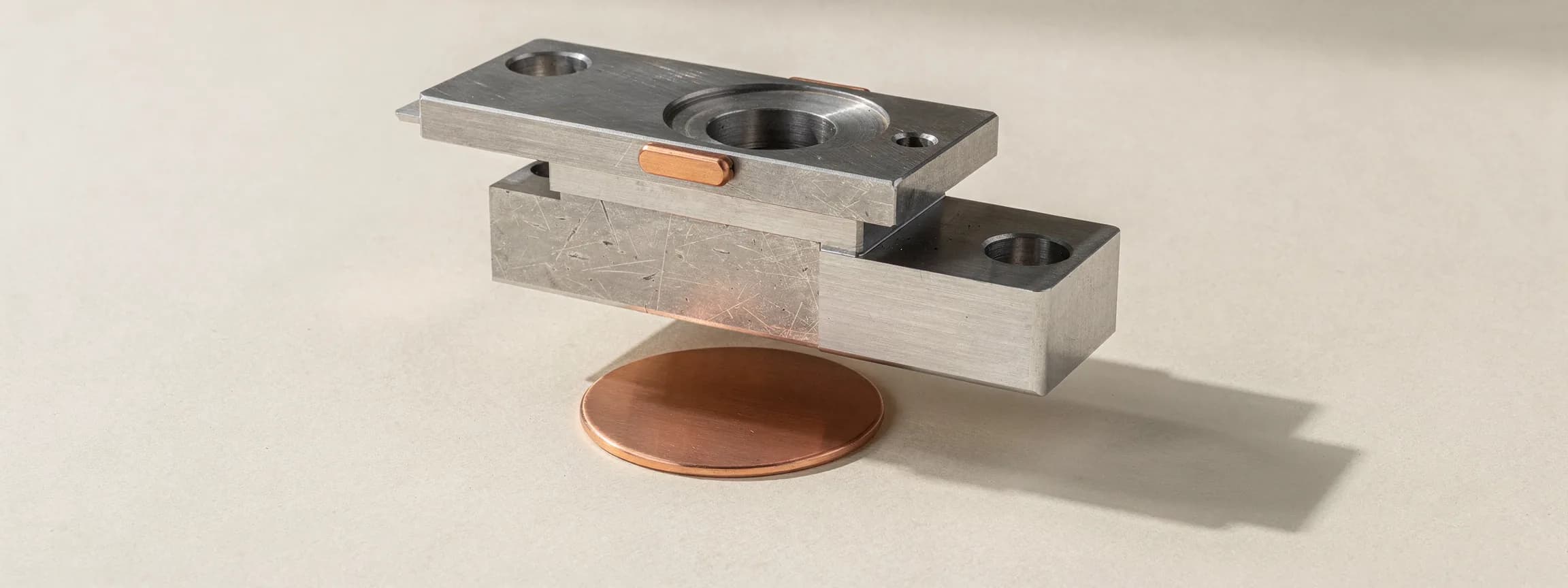 A steel press die with a copper blank beneath it, on paper.