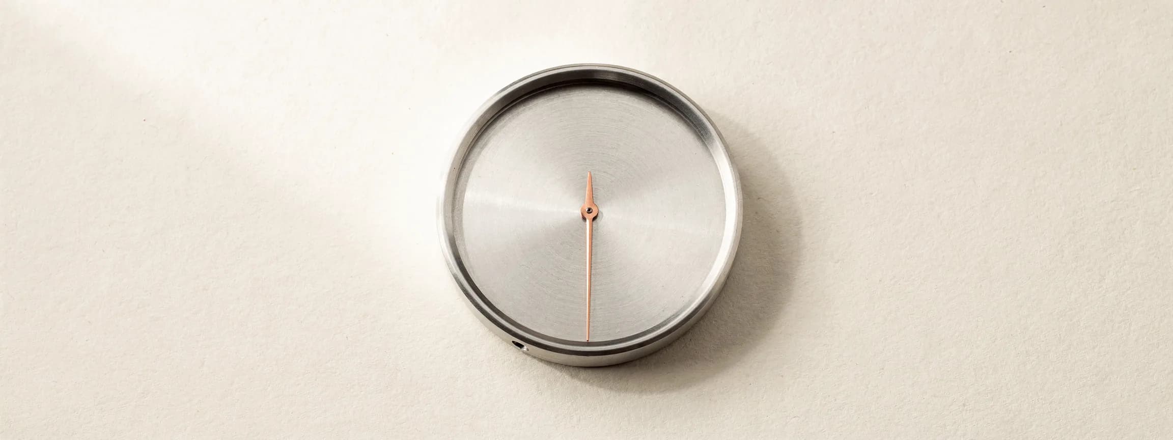 A brushed steel dial gauge with a copper needle, on paper.