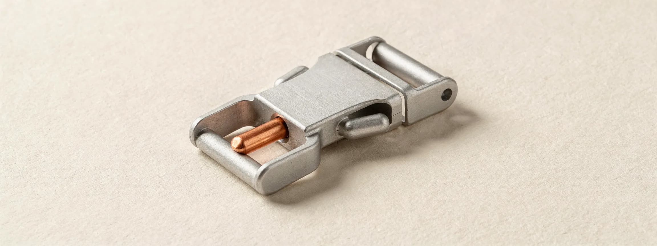 A machined steel harness buckle with a copper pin, on paper.