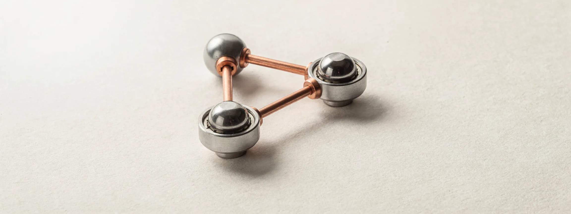 Three polished steel ball bearings joined by copper rods, a small linkage, on paper.