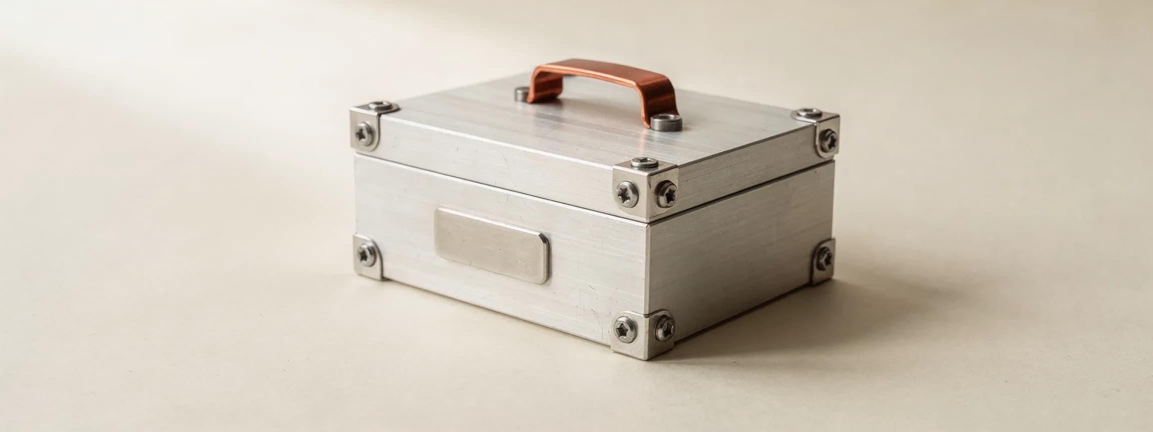 A small machined aluminium crate with a copper handle and a stamped tag, on paper.