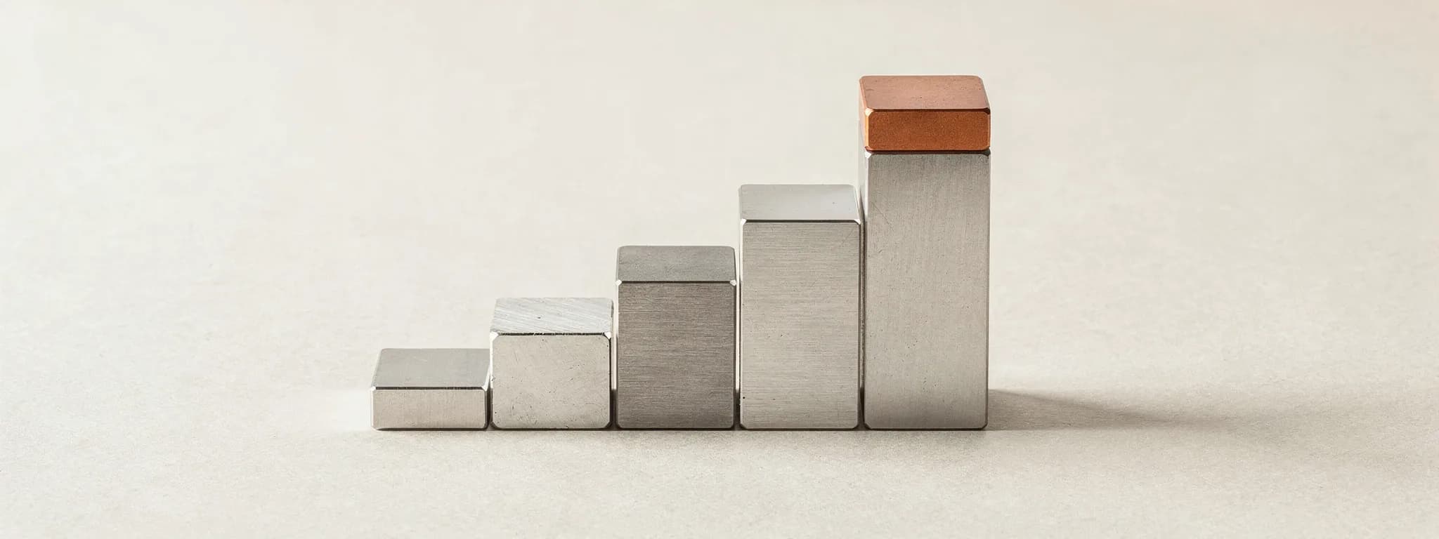 A graduated set of steel gauge blocks rising as steps, the tallest capped in copper.
