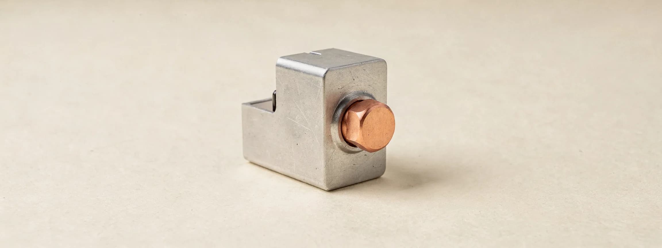 A machined steel tally counter with a copper thumb button, on paper.
