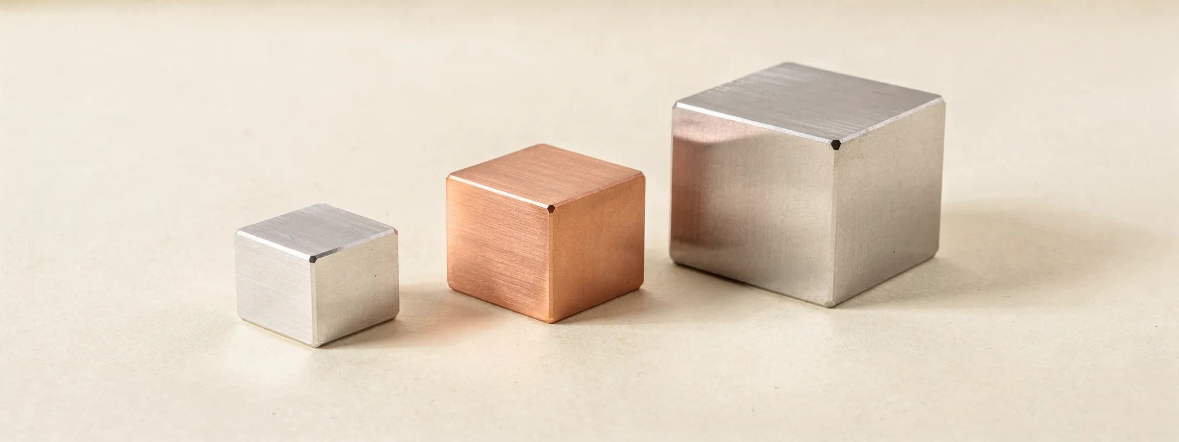 Three machined steel cubes of different sizes, the middle one copper, on paper.